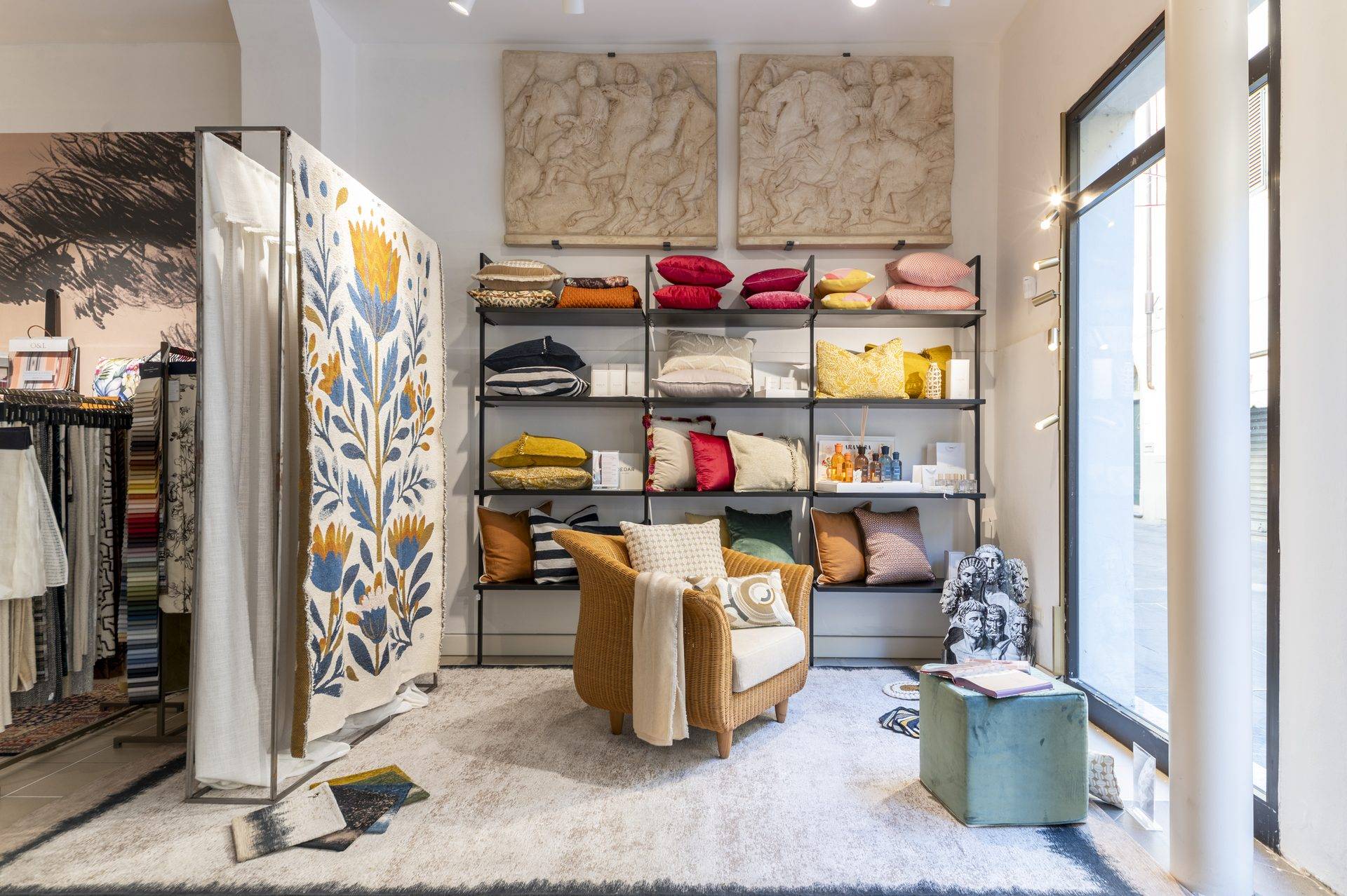 Angolo living nell'atelier Zefiro Interiors a Empoli con poltrona in vimini, cuscini e pannello tessile a fiori