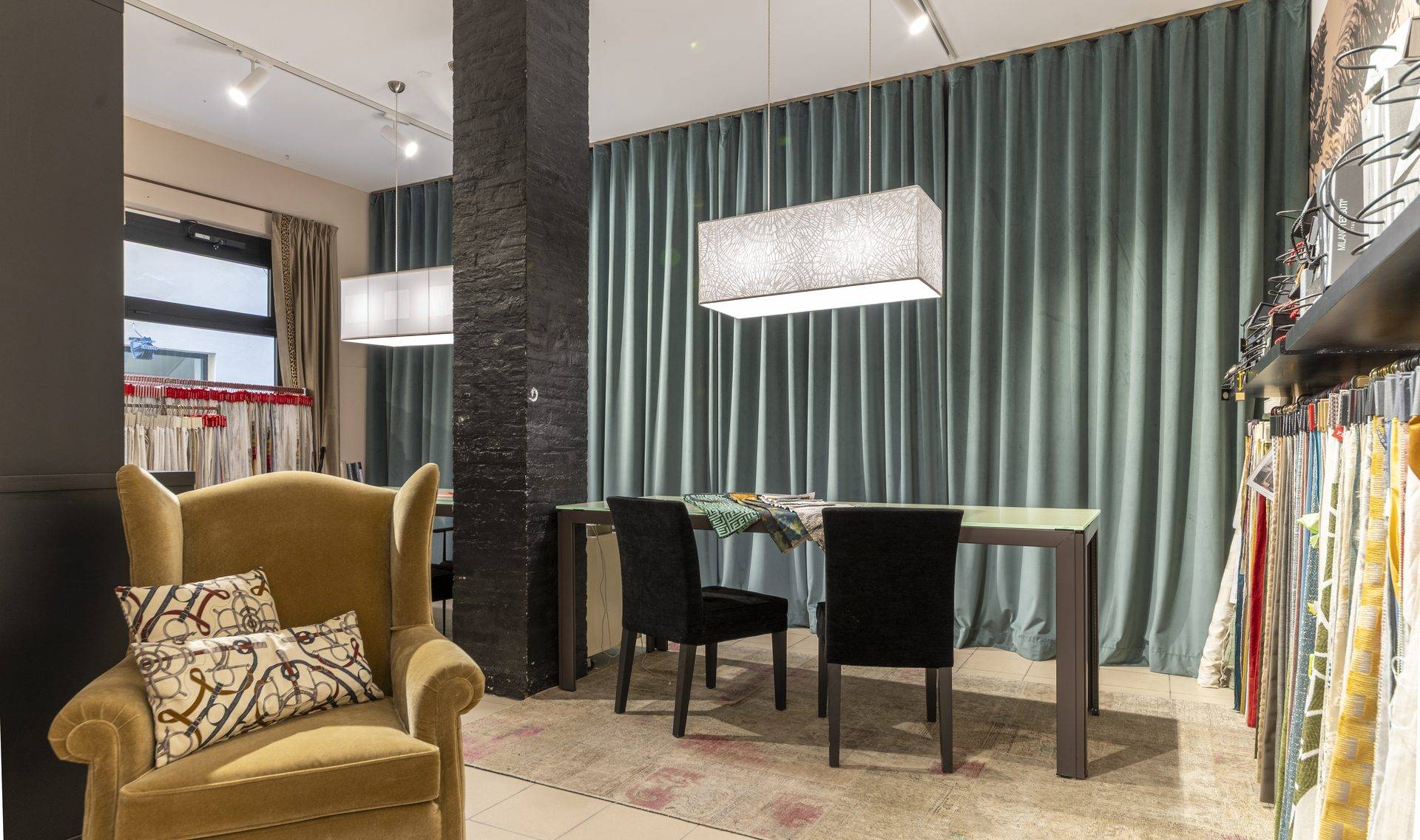 Zona lounge dell'atelier Zefiro Interiors a Empoli con poltrona in velluto, tavolo e tende in velluto color salvia